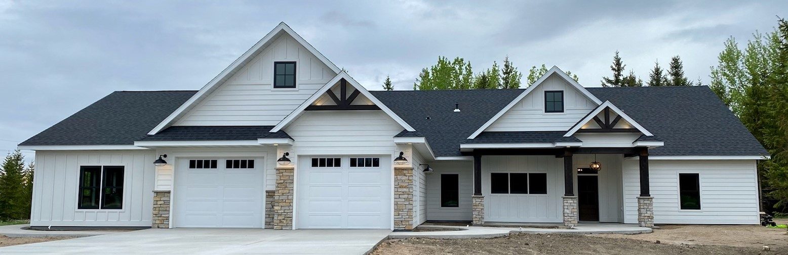 Custom new home build with white board-and-batten farmhouse exterior, statement pillars, and stone column accents in Fergus Falls, MN, supplied by Lakeside Lumber