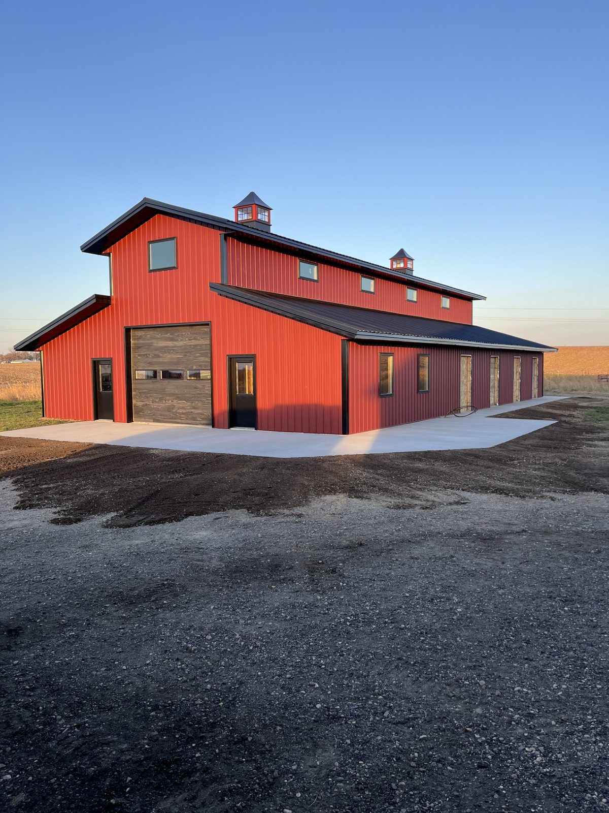 Two-story red post-frame pole barn shop with cupolas and overhead garage door in Fergus Falls, MN, built with materials from Lakeside Lumber