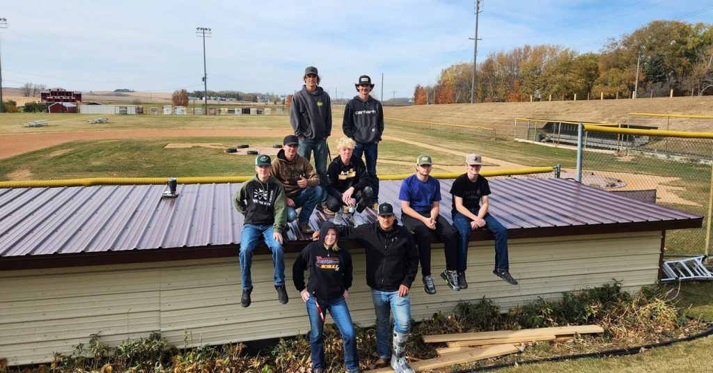 Ashby FFA Manufacturing Exploration students on the finished dugout roof at Ashby baseball field after replacing the sheet metal with materials donated by Lakeside Lumber